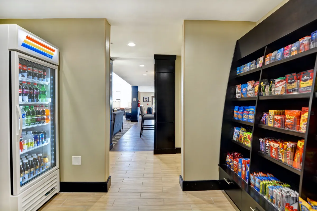 The image highlights a snack area with a vending machine and snack shelves, opening into a hallway that leads to a lounge. The mood is casual and convenient, ideal for grabbing refreshments before heading out or after returning from nearby attractions.