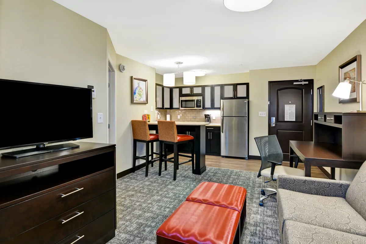 The hero image showcases a bright, inviting condo interior featuring a sleek kitchenette with bar stools, a cozy sofa and coffee table perfect for relaxing, and a flat-screen television ideal for movie nights. The space is designed for comfort and togetherness, with modern amenities highlighted in the open layout.