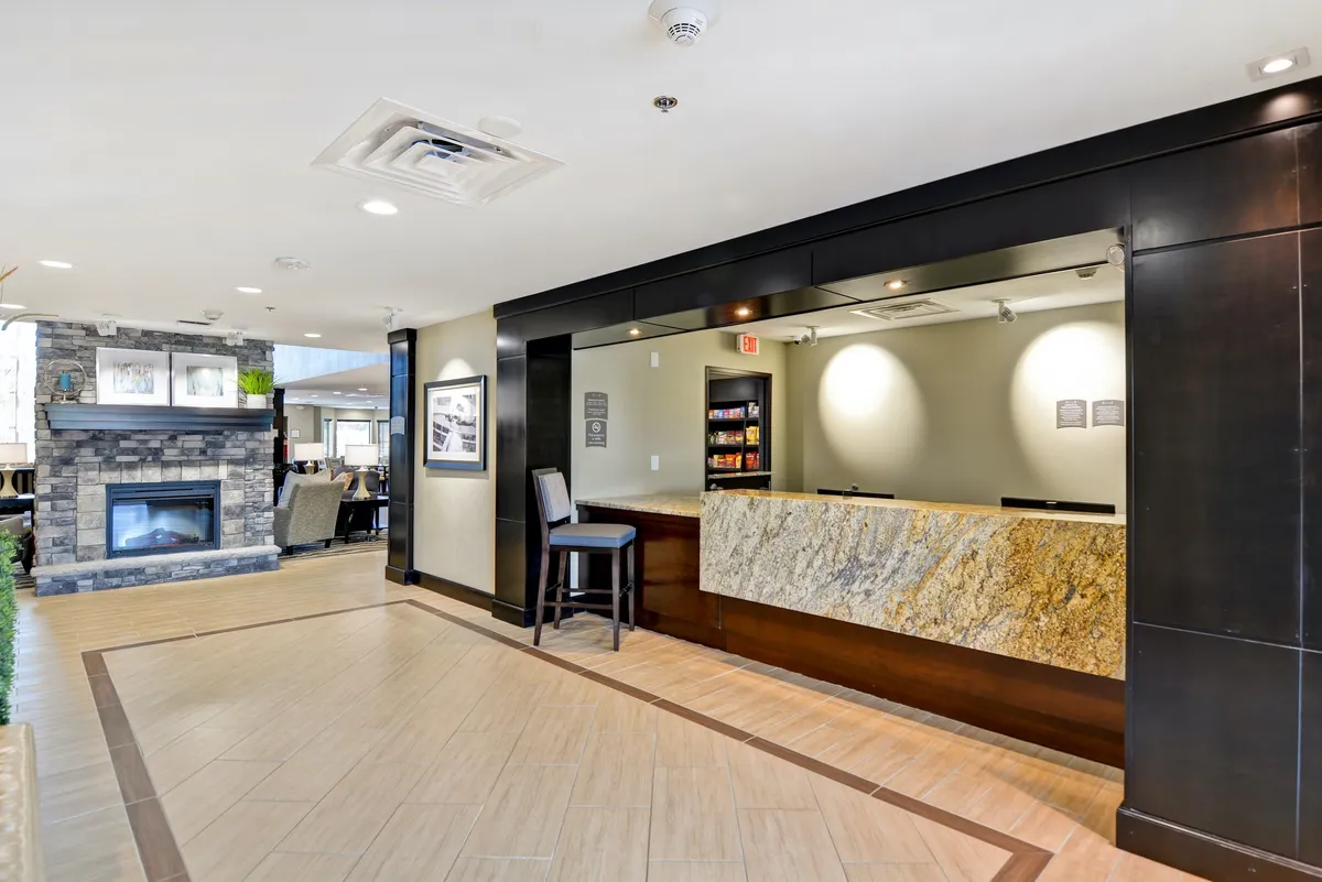 This image captures a warm, inviting lobby scene centered on the reception desk, with a fireplace and comfortable seating area nearby. The lighting and arrangement evoke a sense of welcome and professionalism, highlighting the first point of contact for guests.