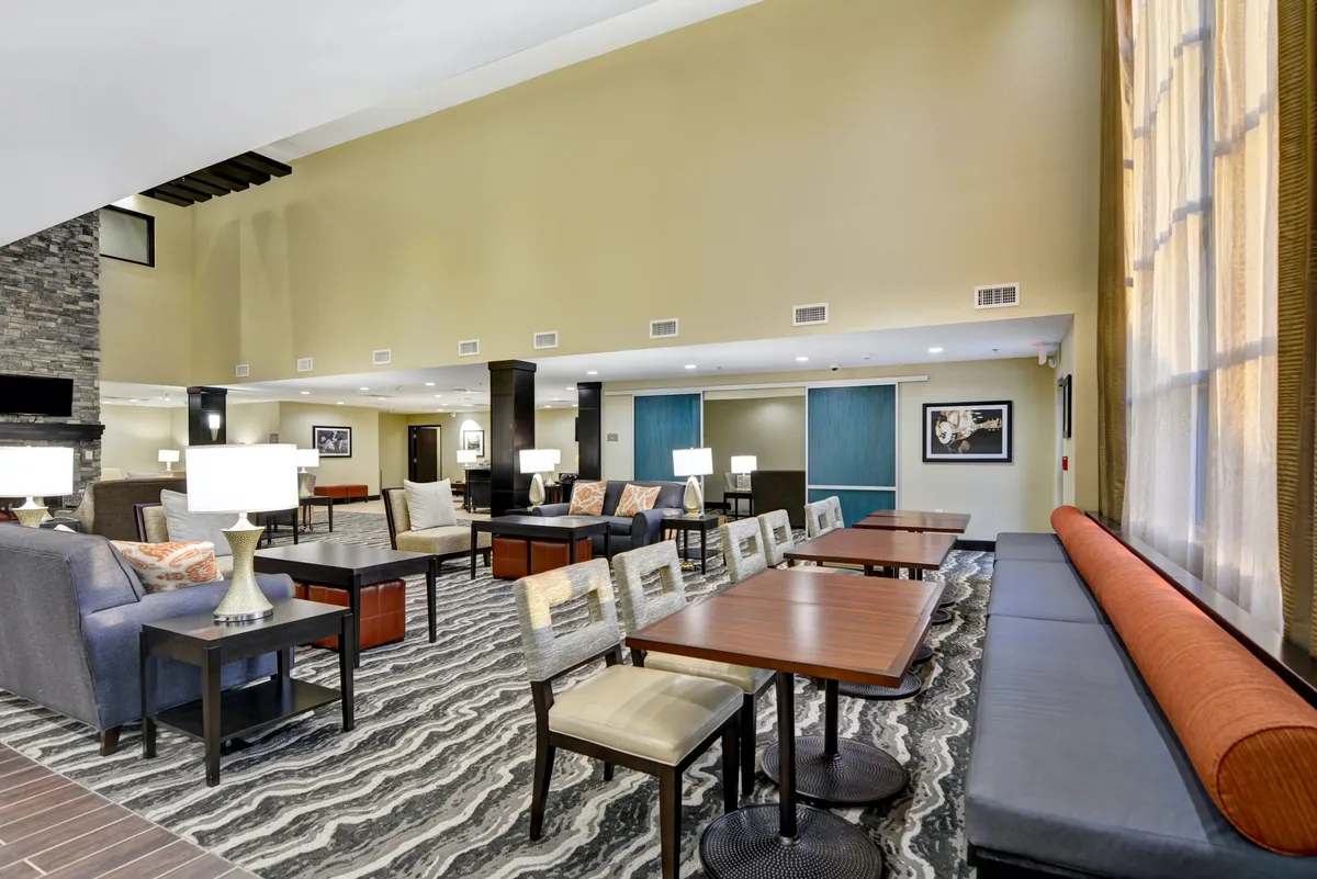 A relaxed communal space with comfortable seating areas and tables, softly lit by decorative lamps. The area is suited for both informal gatherings and focused work on a laptop, capturing a balance between social and productive activities.