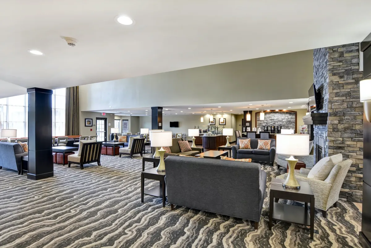 A cozy lounge area featuring plush sofas, warm lighting from lamps, a prominent fireplace, and a soft rug. The environment invites relaxation, reading, or intimate conversations—exemplifying home-like comfort in a communal setting.