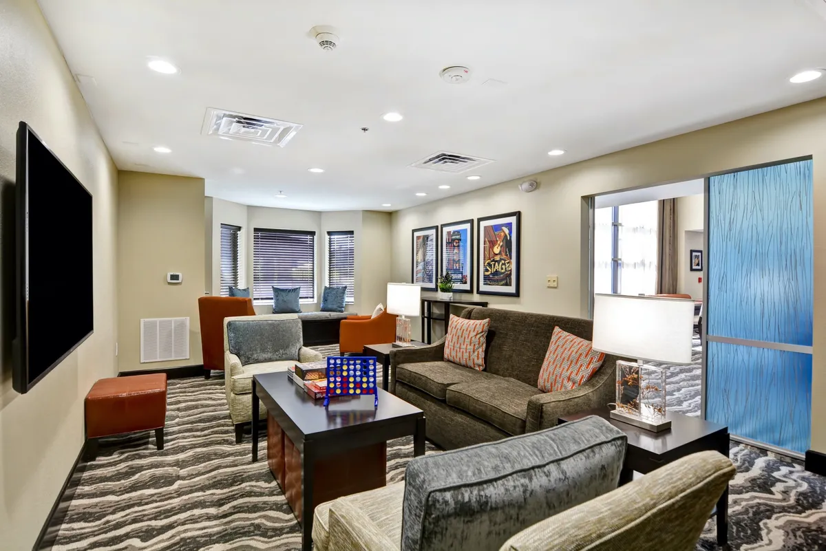 A bright, welcoming living room with a patterned sofa, coffee table adorned with decorative items, contemporary artwork on the wall, and a vibrant blue sliding door. The setup is ideal for relaxing, reading, or socializing.