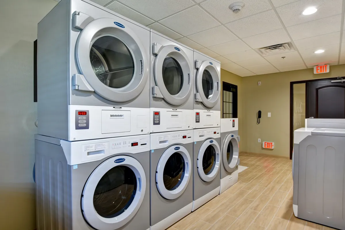 A practical laundry room with stacked washing machines and dryers, illuminated by bright lighting. The area is clean and functional, capturing a sense of convenience for guests staying longer or families needing laundry access.