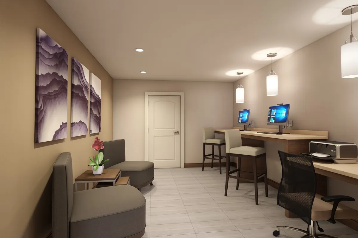 A welcoming communal area with computer stations along the wall, contemporary seating for relaxation, and vibrant artwork. The space is illuminated with soft, practical lighting, inviting guests to work, socialize, or enjoy leisure time.