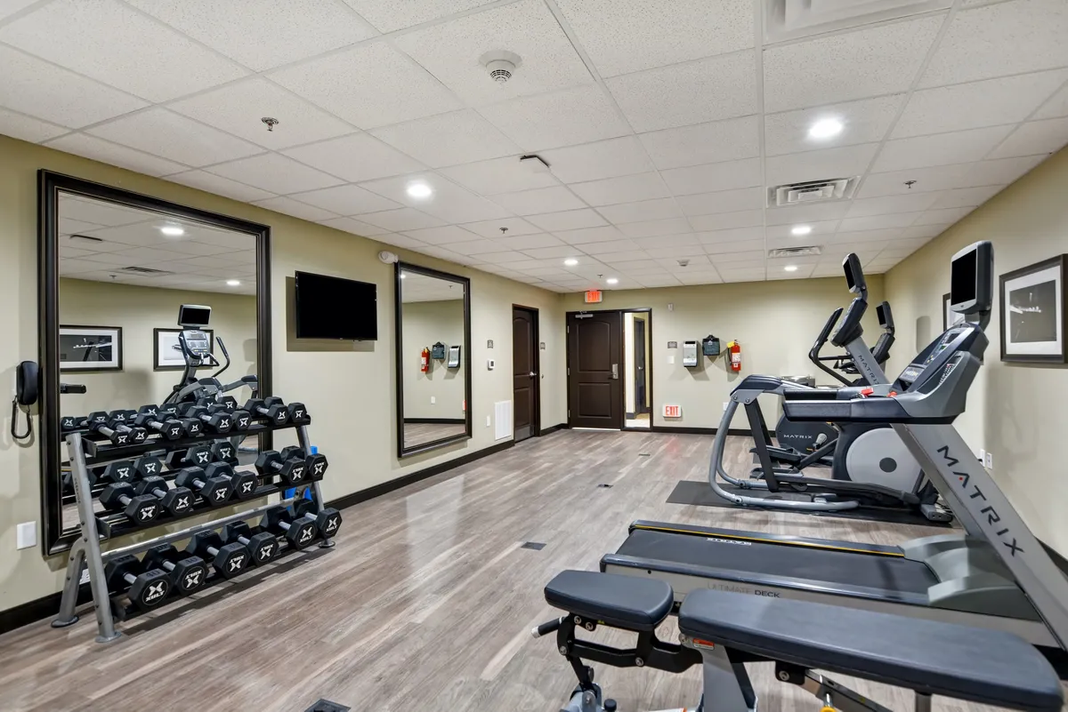 This image presents the property's fitness center, featuring a neatly arranged dumbbell rack, treadmills, and exercise benches. The atmosphere is bright and motivational, suggesting an inviting space for guests to maintain their routines.