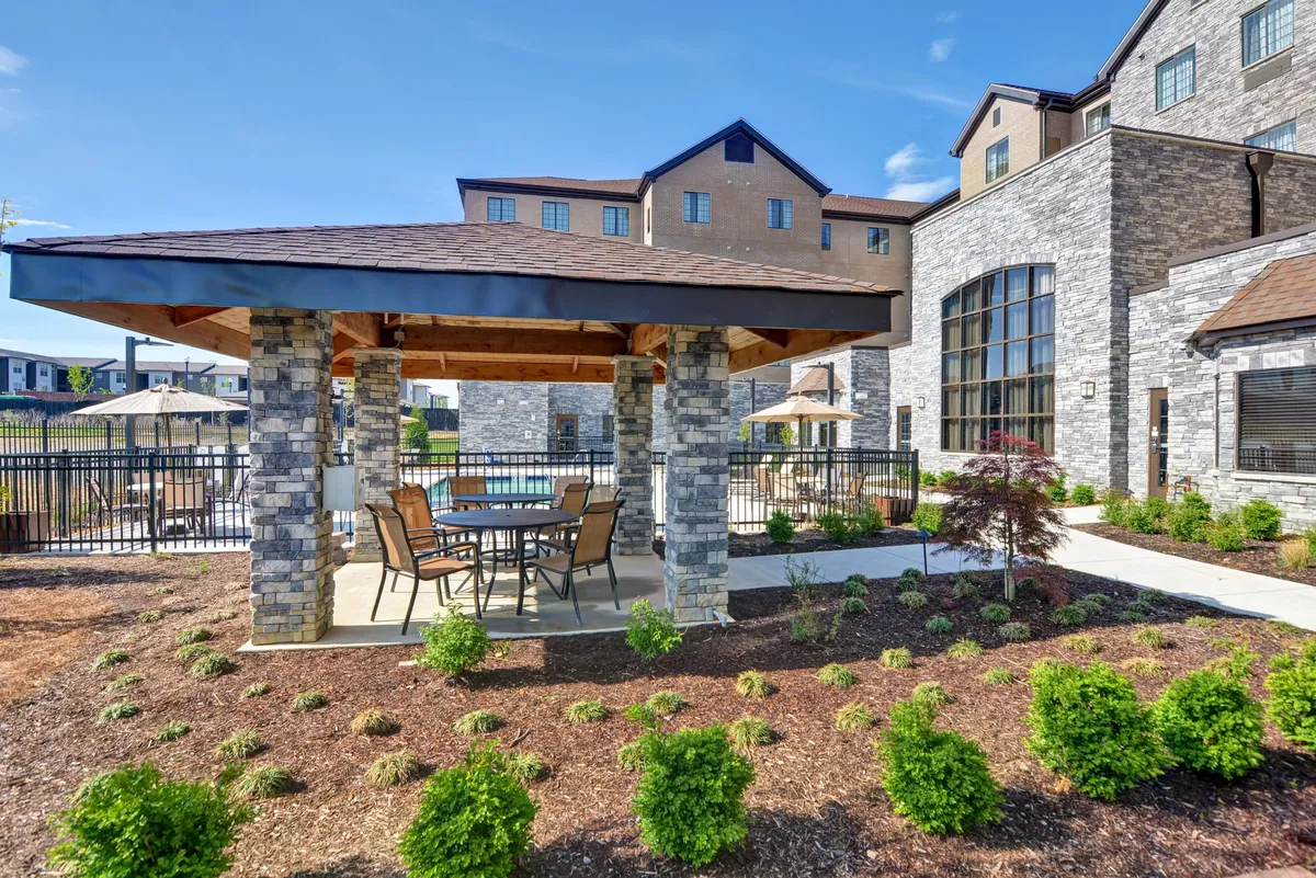 An attractive stone gazebo set amidst lush landscaping, with ample outdoor seating. The area exudes a welcoming atmosphere perfect for social gatherings, outdoor meals, or relaxing after a day out. The scene suggests opportunities for sunset picnics or casual family time outdoors, tying into the narrative of nearby parks and family activities.
